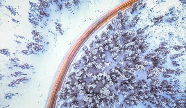 Drone shot of snowy trees and winding road
